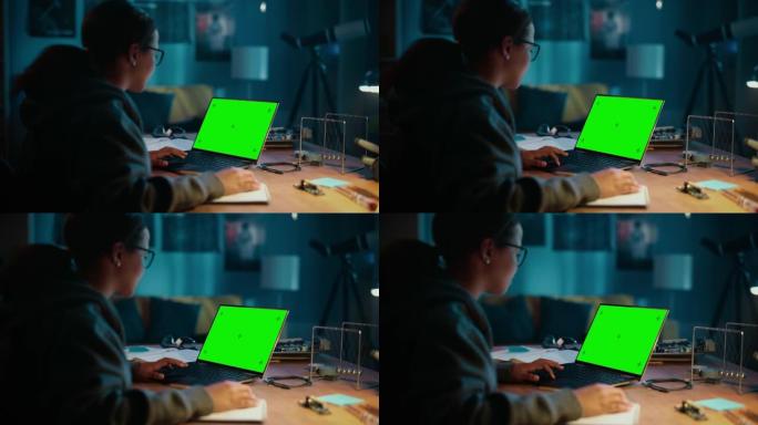 年轻的多种族女孩在家里黑暗舒适的房间里使用带绿屏Chromakey模拟显示的笔记本电脑。她在网上浏览