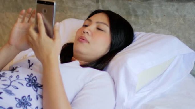 年轻女子在卧室的床上使用智能手机放松和触摸