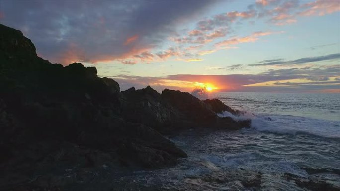 空中: 日落时海浪撞击海滩上的岩石