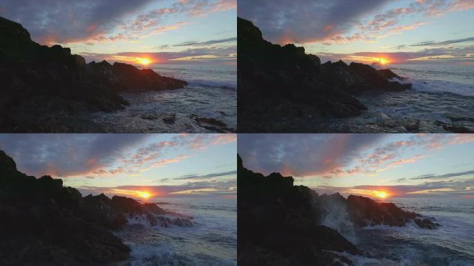 空中: 日落时海浪撞击海滩上的岩石