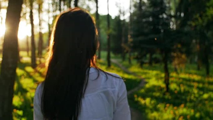 日落时在森林里散步的女人。慢动作