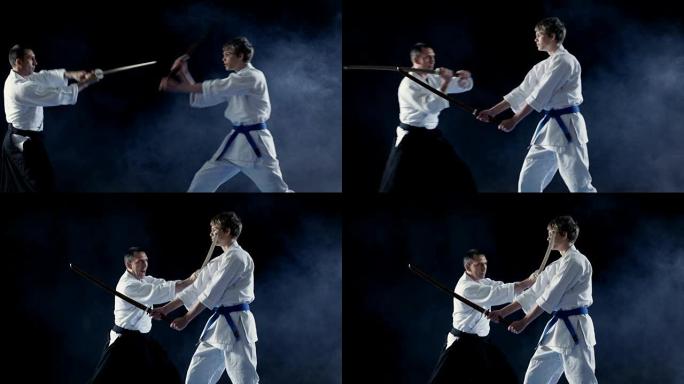 武术大师教他的年轻学生如何用木剑博肯战斗。争吵在几秒钟内结束，大师获胜。拍摄是在黑色背景上隔离的。