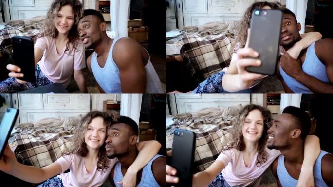 美丽的多民族夫妇在智能手机上拍摄自拍照片。女人拿着智能手机，男人亲吻她并大笑