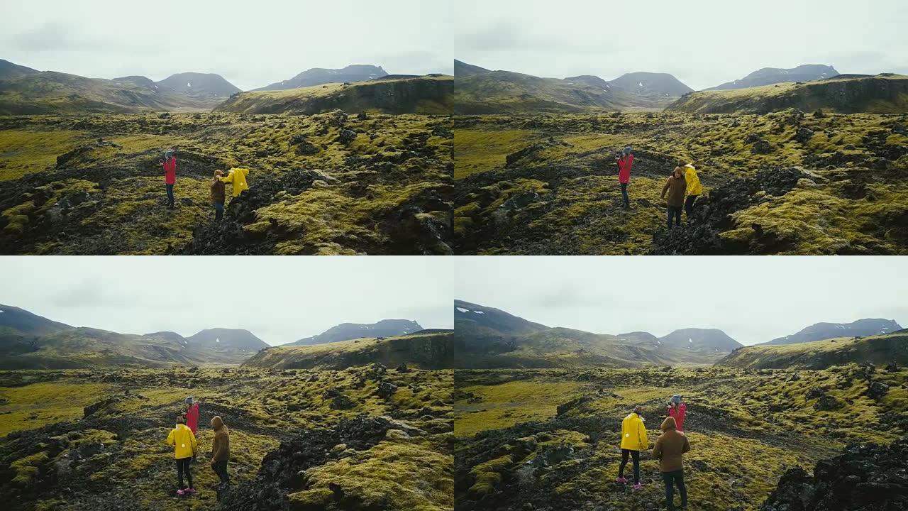 一群游客在冰岛熔岩上徒步旅行的鸟瞰图。女摄影师拿着相机，等着朋友
