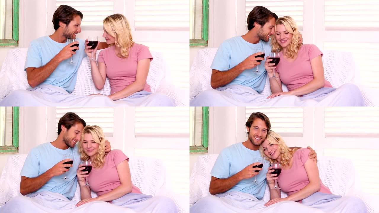 夫妇坐在毯子下的沙发上喝红酒