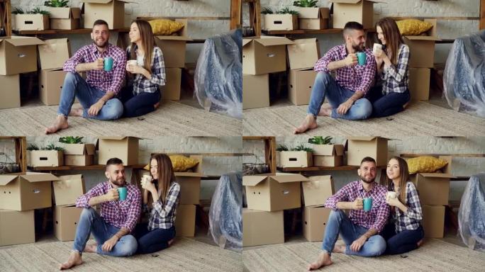 幸福的已婚夫妇同居后，坐在新公寓的地板上，叮当喝着杯子，喝茶。搬迁、年轻人和住房概念。