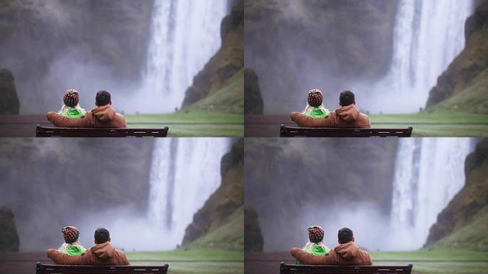 坐在长凳上欣赏冰岛Skogafoss瀑布美景的年轻夫妇的后景