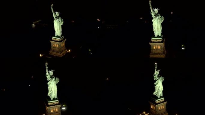 空中特写:著名的自由女神像在夜晚被点亮，在黑暗中闪闪发光
