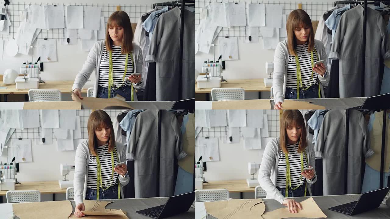服装设计企业家正在检查纸张缝纫草稿并查看智能手机。她正在仔细检查每个切口，并考虑未来的服装。