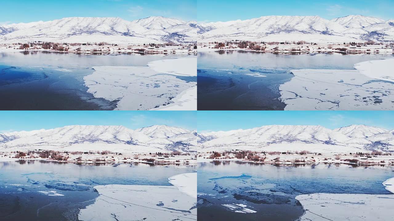 鸟瞰图飞越冬季湖，冰雪覆盖，背景为雪山