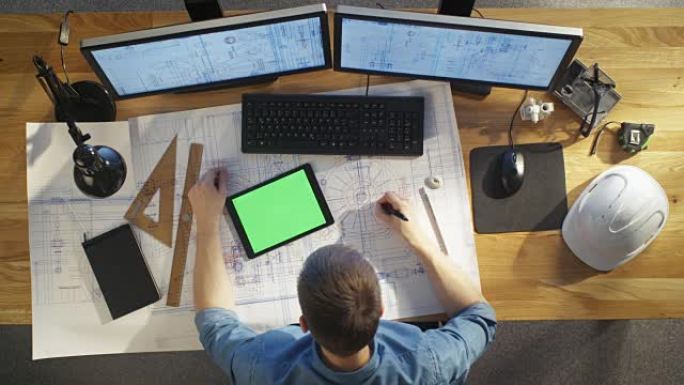 建筑工程师的俯视图借鉴了他的蓝图，与绿屏平板电脑相比，还使用台式电脑。他的桌子上摆满了有用的物品和傍