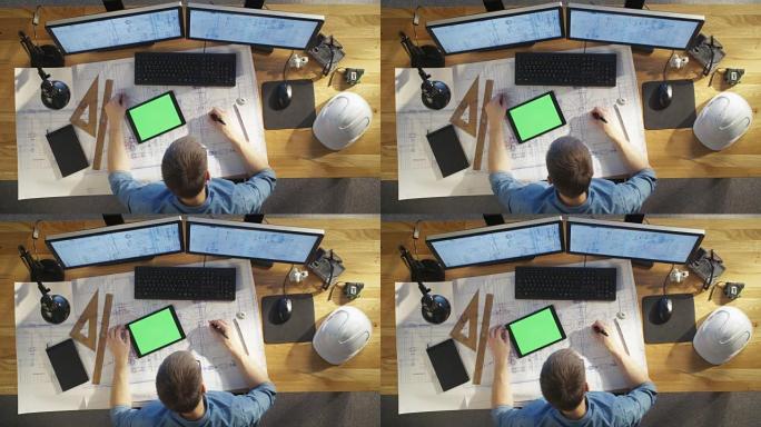 建筑工程师的俯视图借鉴了他的蓝图，与绿屏平板电脑相比，还使用台式电脑。他的桌子上摆满了有用的物品和傍