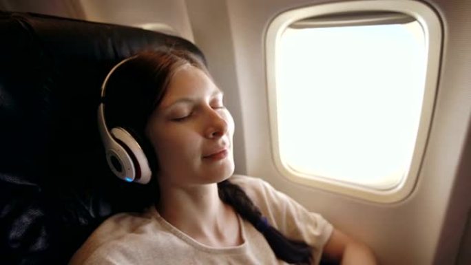 戴着无线耳机的年轻女子在飞机上听音乐和微笑
