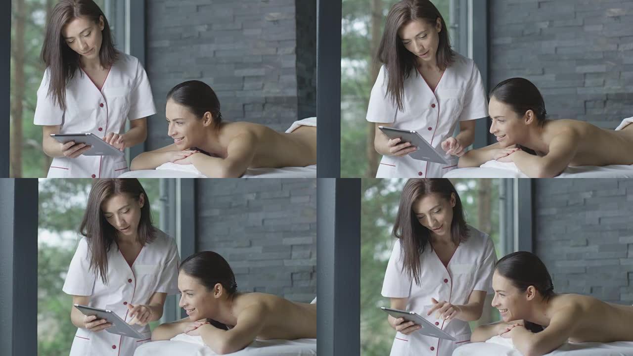 女按摩师在健康中心的放松过程中向顾客展示平板电脑。