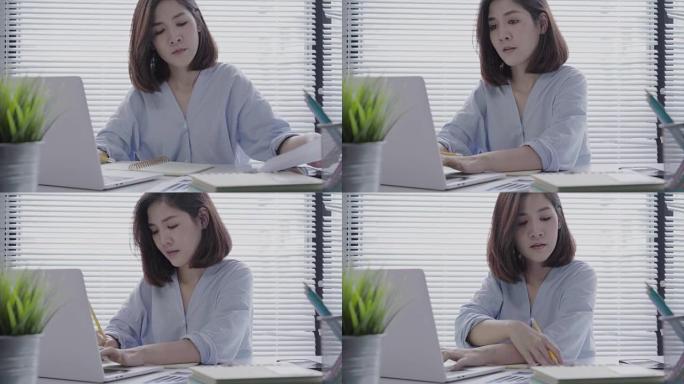 美丽的年轻微笑的亚洲女人坐在家里的客厅里在笔记本电脑上工作。在家庭办公室工作的亚洲女商人。在家享受时