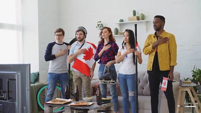 多民族的朋友一起听和唱加拿大国歌，然后一起在家看电视上的体育比赛
