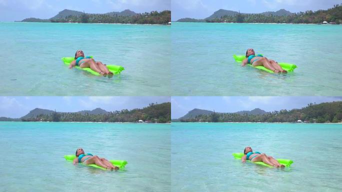 慢动作:年轻女子放松在充气水床漂浮在美丽的波拉波拉岛在阳光明媚的夏天完美的蓝色泻湖