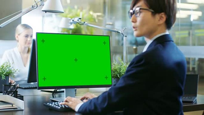 在办公室里，东亚商人在一台带有模拟绿屏的台式个人计算机上工作。他戏剧性地转过头，看着肩膀对着镜头。同