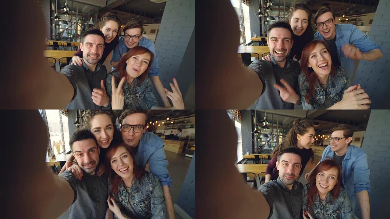 在咖啡馆摆姿势，微笑拥抱和打手势的欢快的一群朋友录制有趣的视频的视点镜头。友谊和幸福的人的概念。
