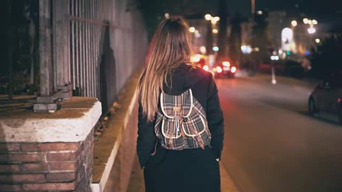 背着背包的黑发女人深夜散步。迷人的女孩晚上穿过市中心，靠近马路
