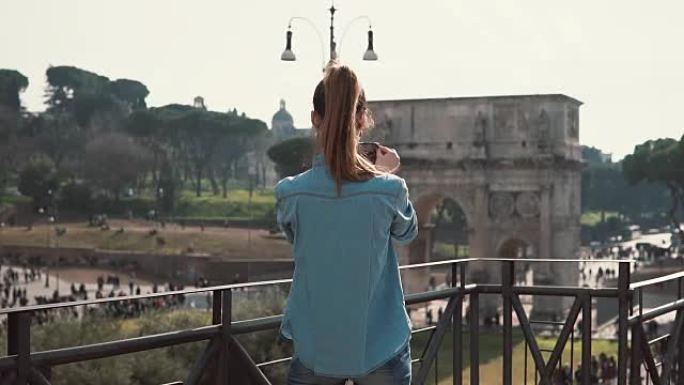 在阳光明媚的日子里，年轻女子在意大利罗马用智能手机拍摄君士坦丁拱门的照片。慢动作