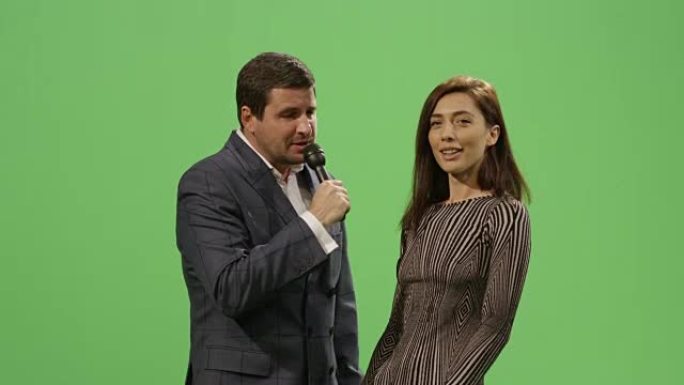带麦克风的媒体记者正在后台的模拟绿屏上采访一名穿着连衣裙的女子。