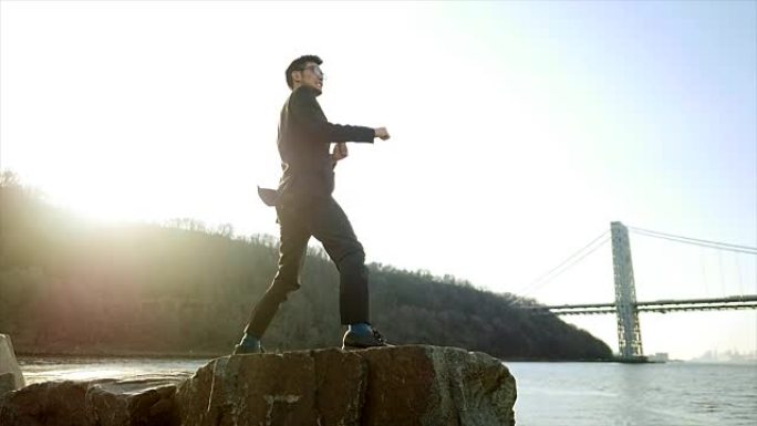 亚洲人独自站在海边的岩石上。做空手道训练。走在石头。象征着成功、独立、克服障碍