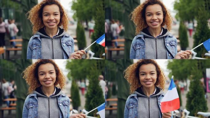 夏天，美丽年轻的非洲裔美国妇女举着法国国旗，微笑着看着相机。快乐的游客和千禧一代的概念。