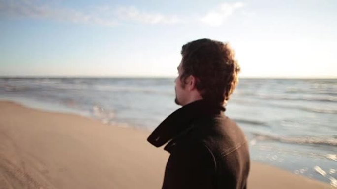 一个穿着黑色外套的黑发年轻人的侧视图正在海边行走