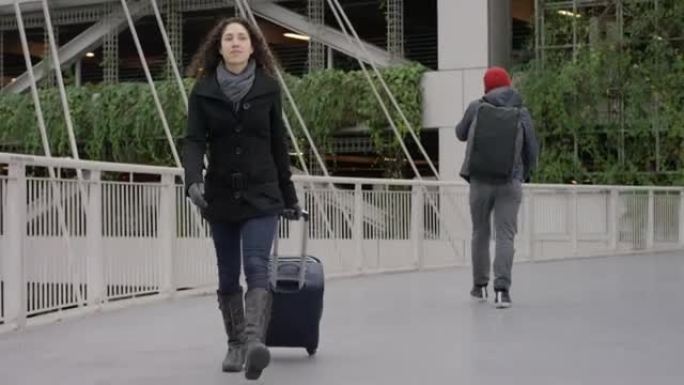 年轻的少数民族女性拉着行李箱穿过机场天桥