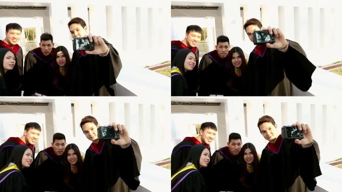 一群穿着砂浆板和单身汉礼服的快乐国际学生，带着文凭在户外用小型相机自拍。教育、毕业、技术和人的概念。