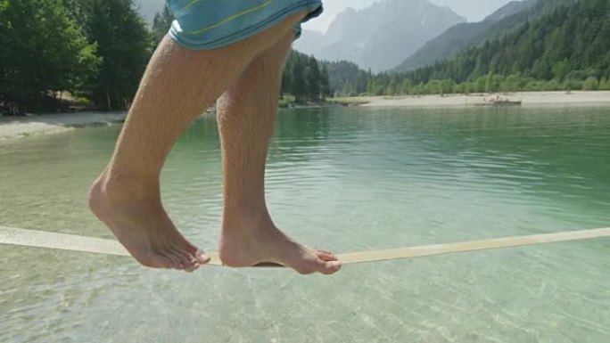 慢动作特写: 在阳光明媚的夏天，穿着泳衣的年轻男性在湖面上方的松弛线上行走和平衡