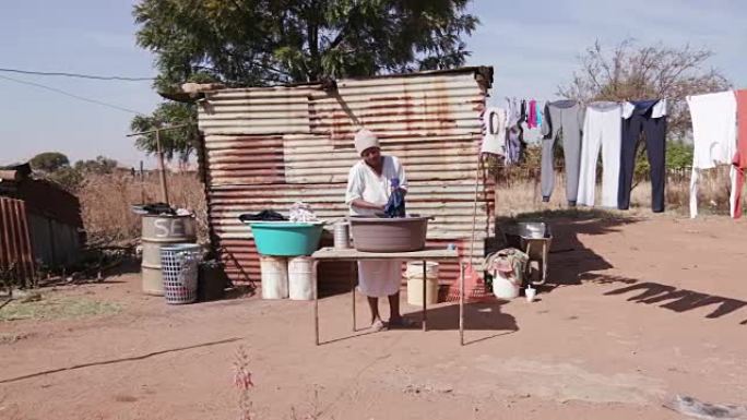 没有自来水的非洲妇女在锡棚屋前的水桶里洗衣服