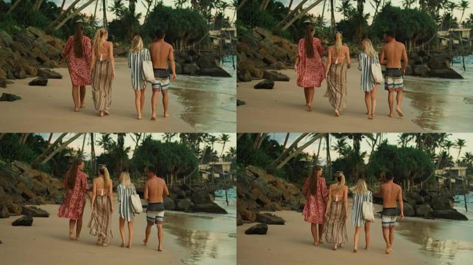 在三个漂亮的女孩和一个英俊的男人沿着海滩散步的镜头之后。甜美的绿色森林，面前有棕榈树。