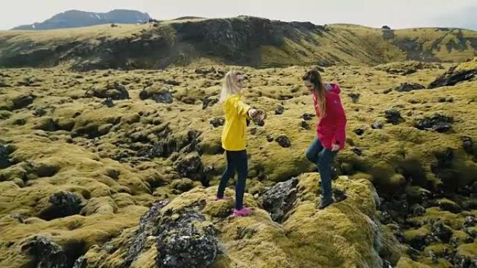 两个女人站在岩石上的鸟瞰图，看着冰岛的熔岩田野跳舞，感到自由，幸福