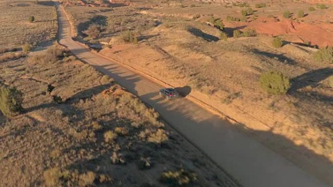 空中的黑色吉普车沿着尘土飞扬的道路穿过阳光灿烂的灌木丛峡谷