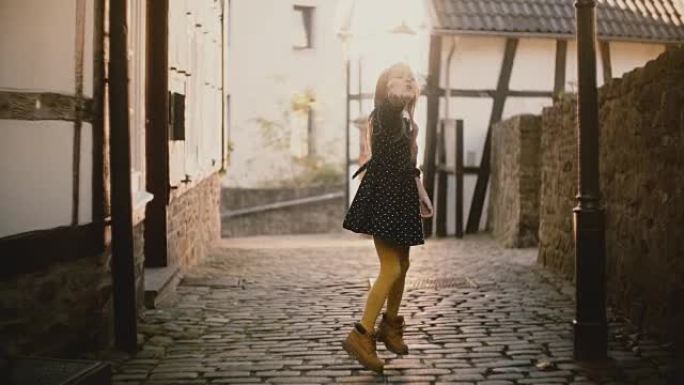 可爱的高加索女孩吹吻的肖像。快乐的女孩子在铺好的街道上对着镜头摆姿势。阳光耀斑。4K