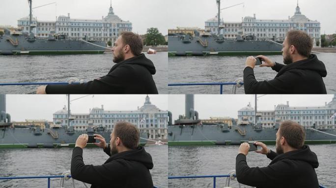 圣彼得堡观光。英俊的男人探索，拍摄巡洋舰Aurora的照片，使用他的智能手机，慢速