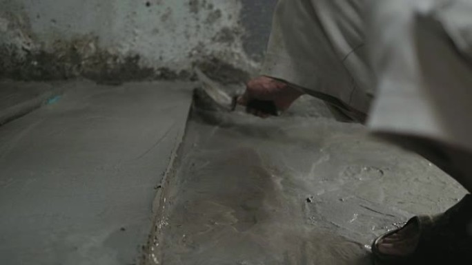 男人的手用抹刀抹平地板。建筑工人在家。
