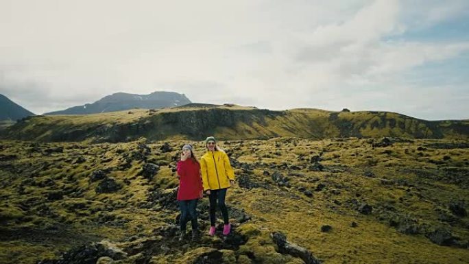 鸟瞰图中冰岛熔岩场的两名女子举起了手。快乐的游客送飞吻直升机