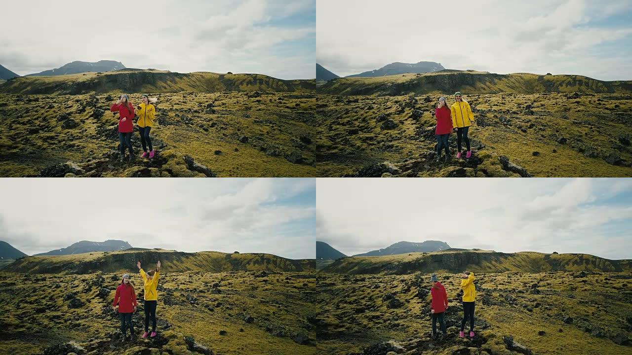 鸟瞰图中冰岛熔岩场的两名女子举起了手。快乐的游客送飞吻直升机