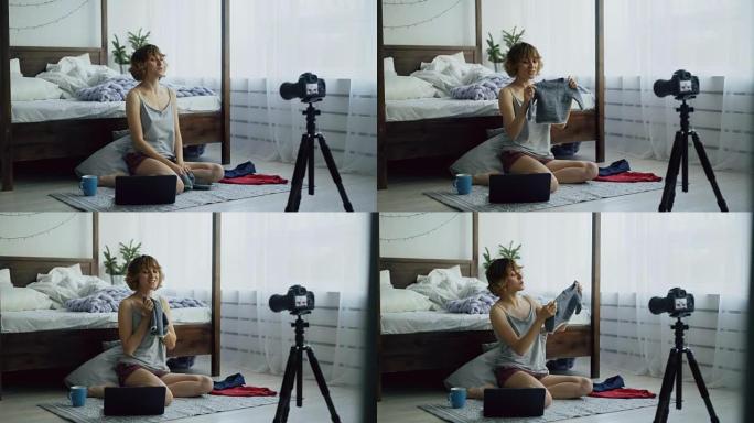 迷人开朗的女人坐在床边录制视频博客关于家里有dslr相机的童装
