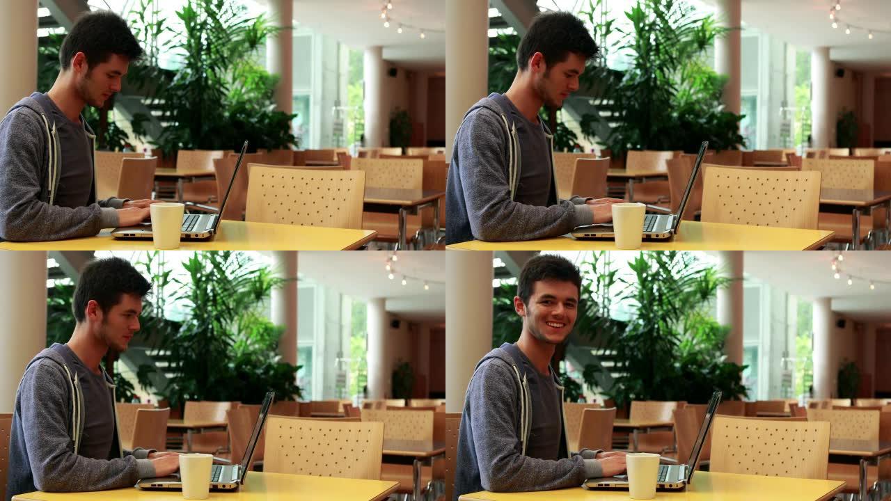 微笑的学生坐着使用他的笔记本电脑