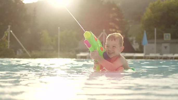 慢动作特写: 美丽的金色日落时，浅水公园的小男孩用有趣的水枪瞄准和射击