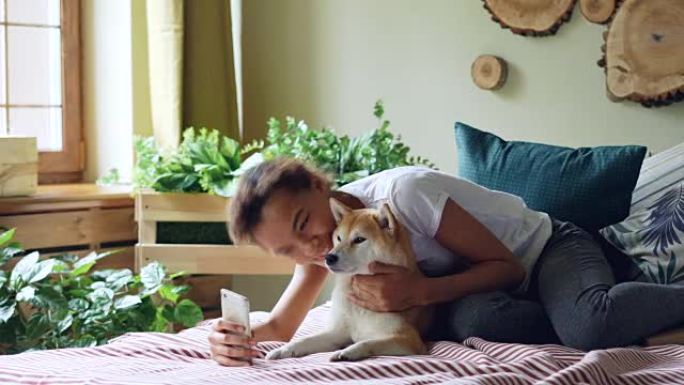 漂亮女孩骄傲的狗主人正在打视频电话，爱抚躺在家里床上的纯种狗，年轻的女人正在说话，并向对话者展示动物