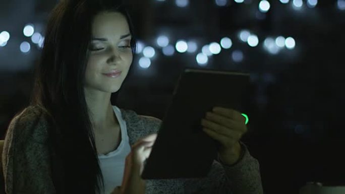笑容灿烂的少女在晚上使用平板电脑。休闲生活方式。