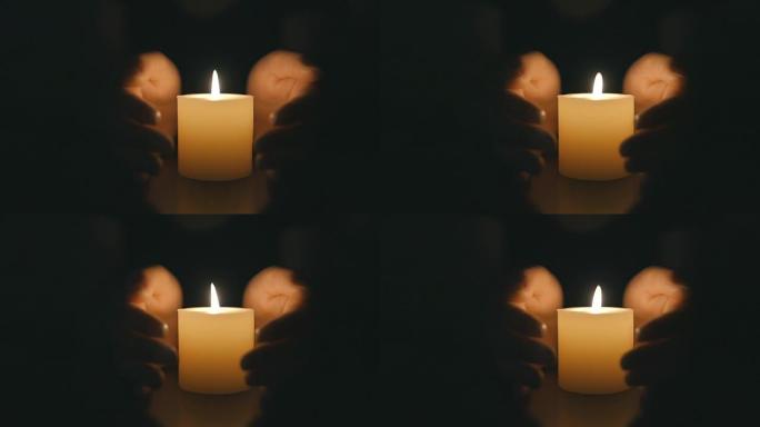 双手保护黑暗中燃烧的蜡烛烛光