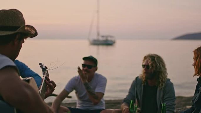 朋友在日落海滩上闲逛喝啤酒和弹吉他，慢动作