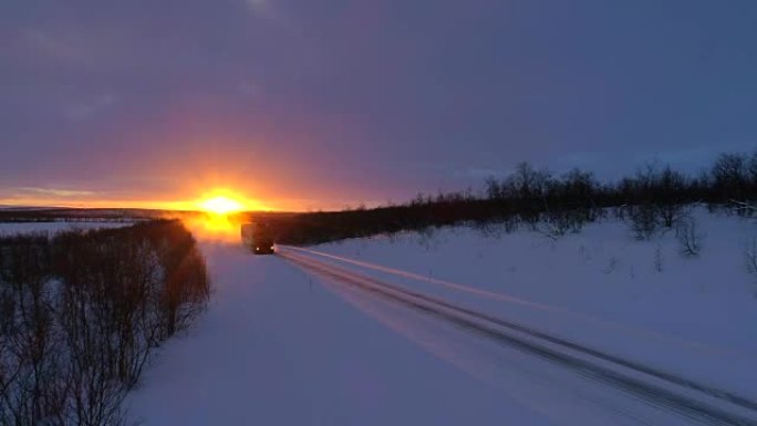 日落时，半卡车在积雪覆盖的公路槽森林景观上行驶