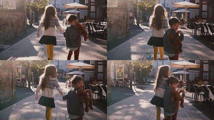 小女孩和男孩手牵手走在一起。慢动作。后视图。两个孩子在阳光明媚的日子里在老城区四处游荡